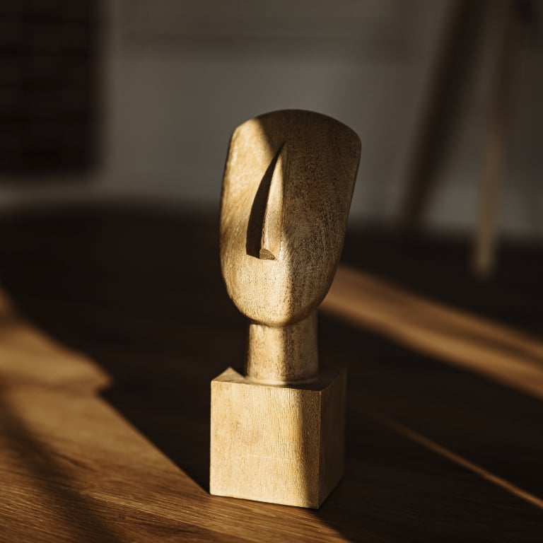 Eine Holzskulptur mit stilisiertem Kopf, die zur Hälfte im Schatten liegt (Symbol für Depression)