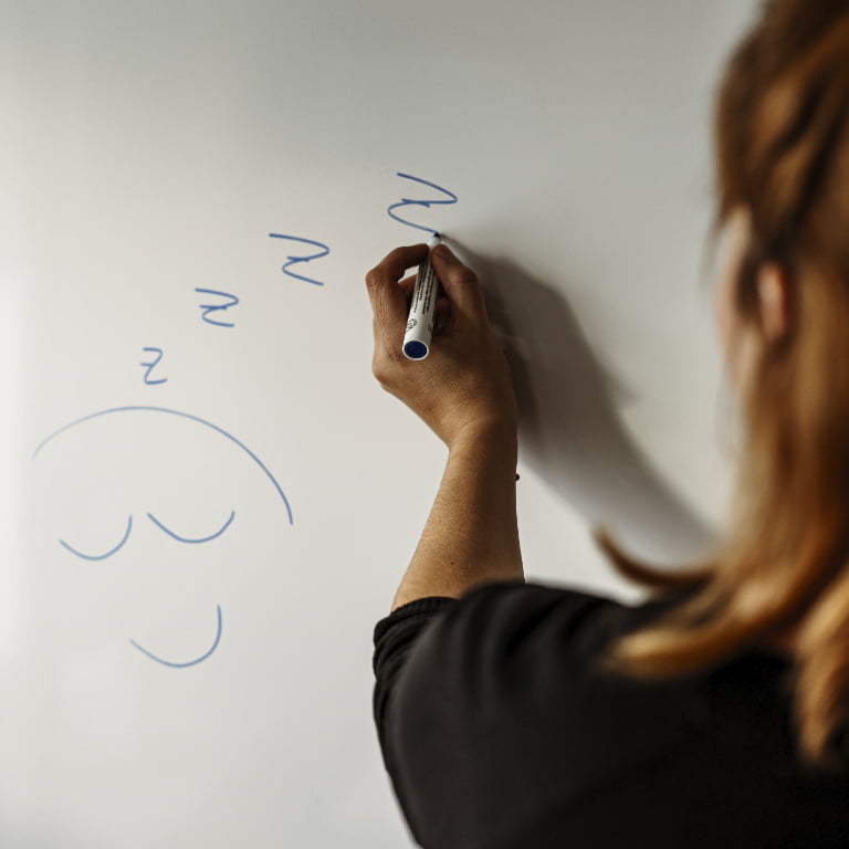 Julia Rosenberg, die auf ein Whiteboard ein schlafendes Gesicht malt (Symbol für Schlafstörungen)