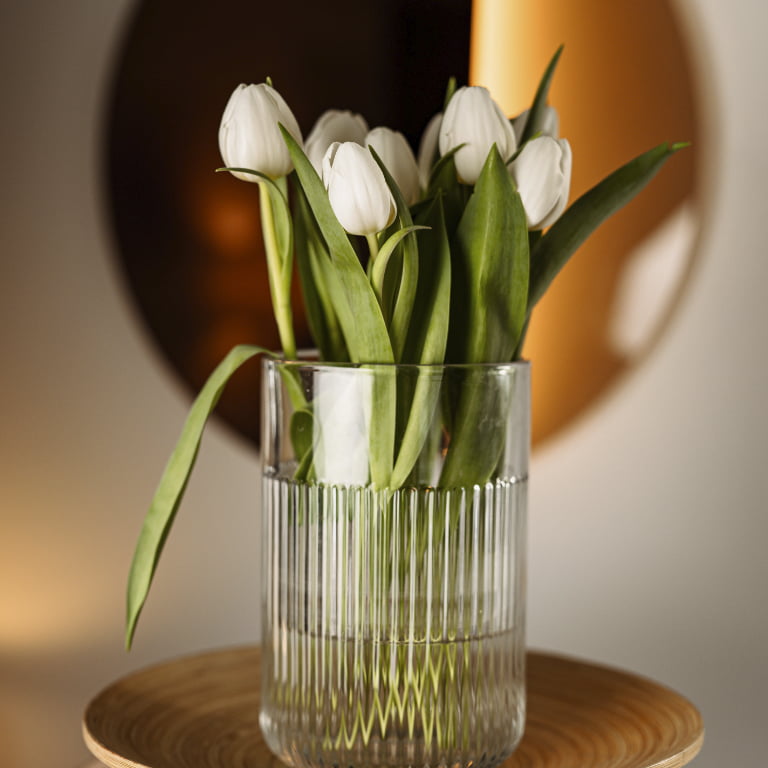 Eine Glasvase auf einem Holztablett mit weißen Tulpen (Symbol für Traumafolgestörungen)