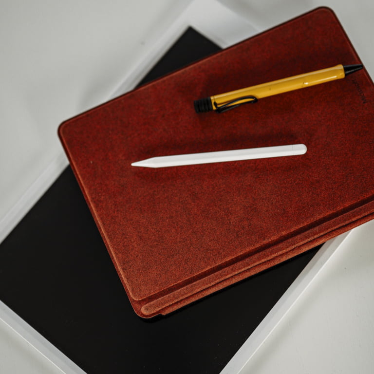 Ein Notepad und ein Tablet mit roter Hülle. Darauf liegen ein weißer Notepadstift und ein gelber Kugelschreiber. 